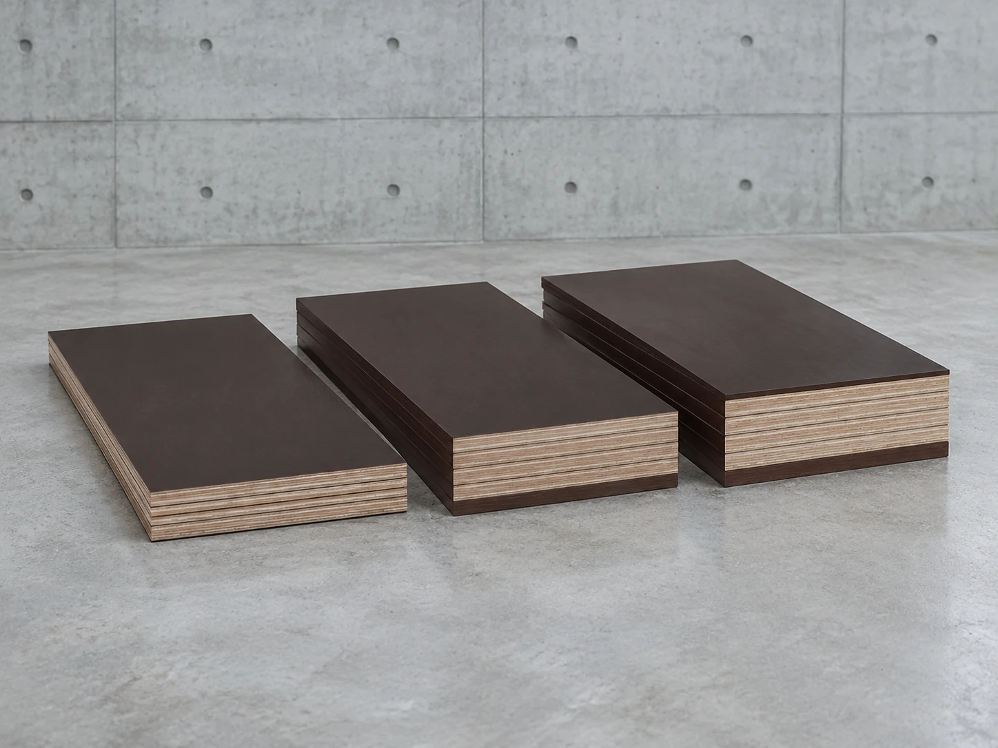 Three short stacks of film-faced plywood pieces in different thicknesses side by side on a concrete floor