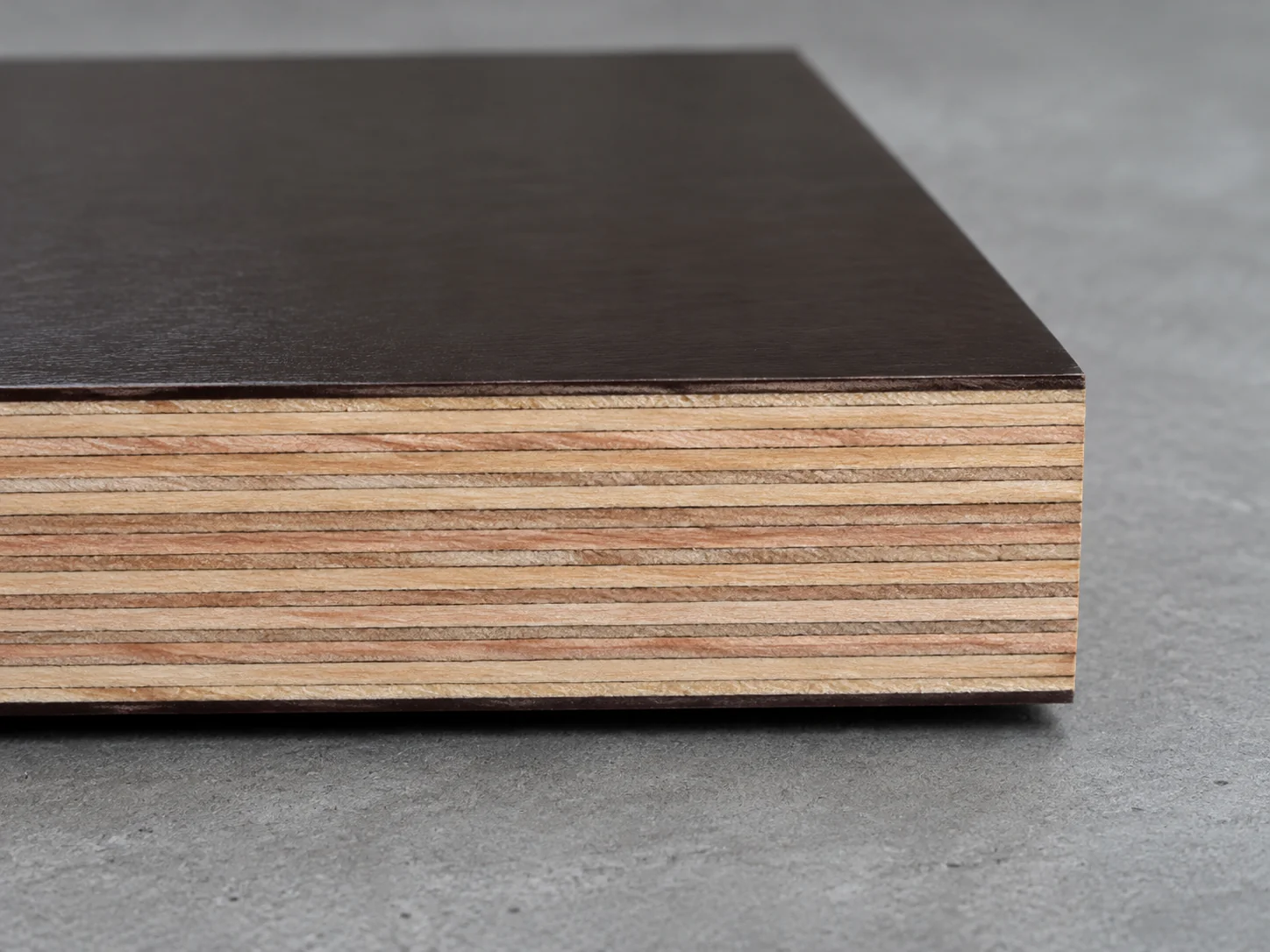 Cut edge of film-faced plywood with thin dark film on both faces and pale hardwood veneer layers