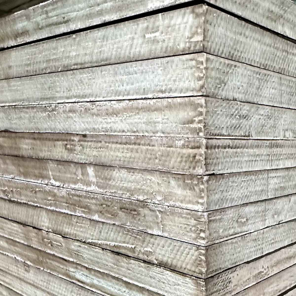 Corner of a plywood stack before edge sealing, showing many pale veneer layers on two sides
