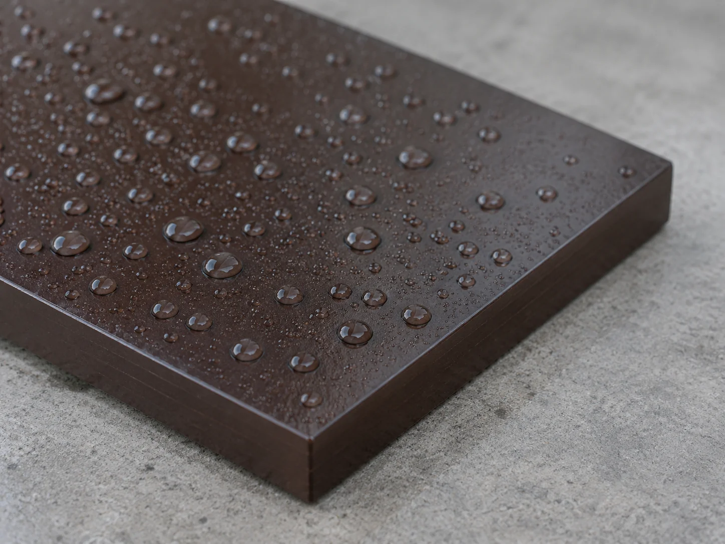 Water droplets beading on the dark brown film face of a plywood panel next to its sealed edge