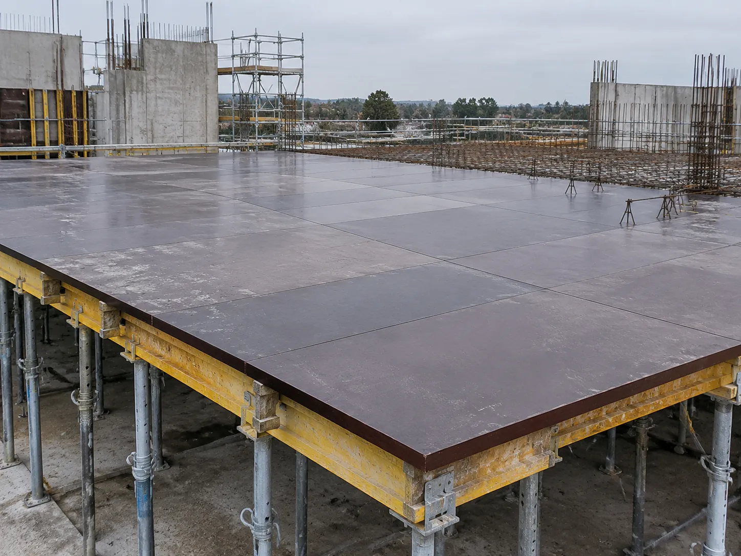 Slab formwork deck of separate film-faced plywood sheets with visible joints and concrete stains, on timber beams and steel props