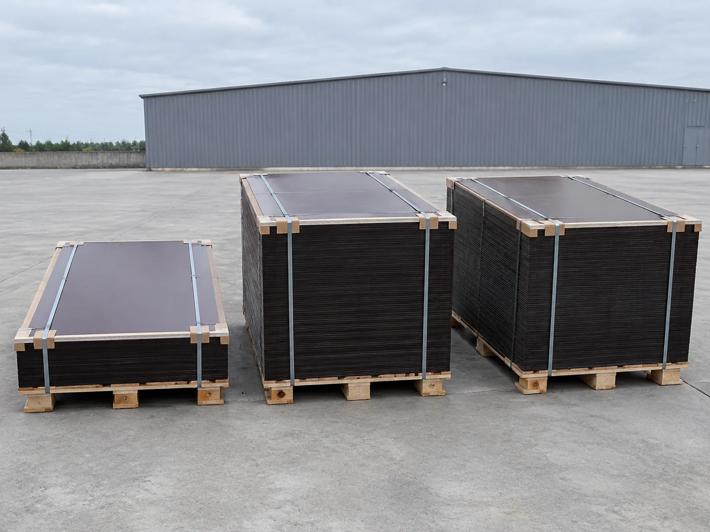 Three strapped export bundles of film-faced plywood on wooden skids in a concrete yard